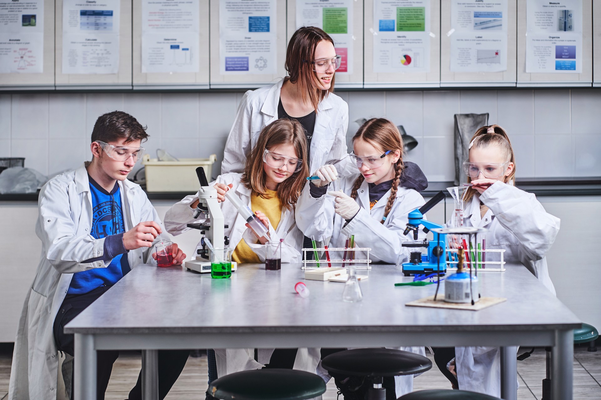 Dzieci w fartuchach laboratoryjnych przeprowadzają eksperymenty naukowe z mikroskopami